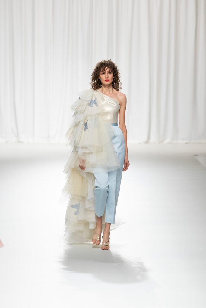 A fitted blue and cream asymmetric dress with layered tulle detailing and a high neckline.