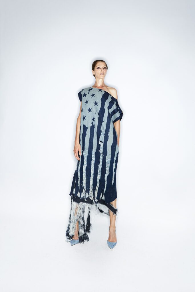 A relaxed blue denim off-shoulder dress with an asymmetric hem and fringed details.