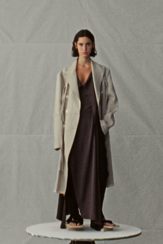 A fitted black dress layered under a beige coat with a V-neckline and asymmetric design.