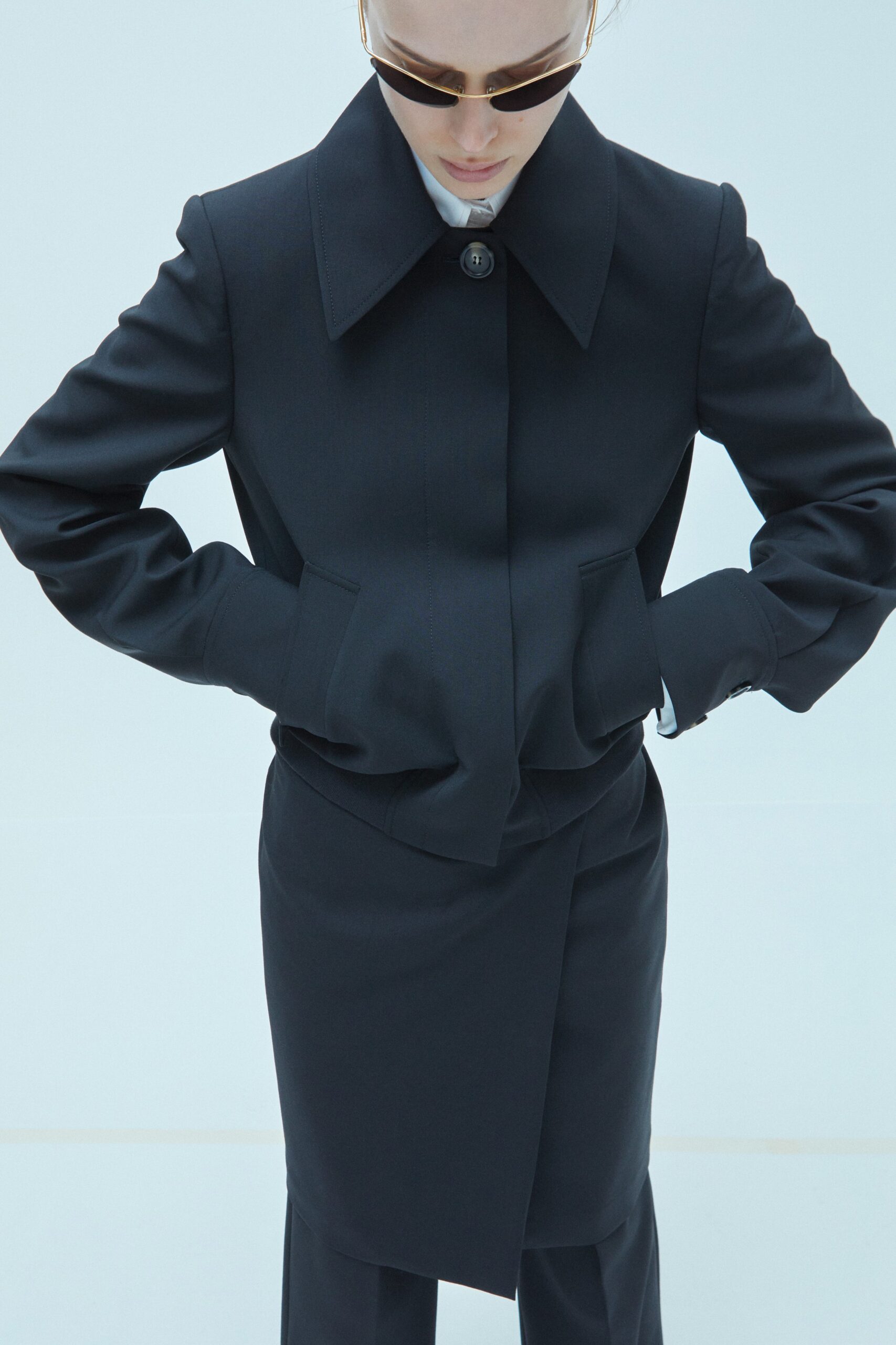 A structured black wool coat with long sleeves and a collared design, featuring button details.