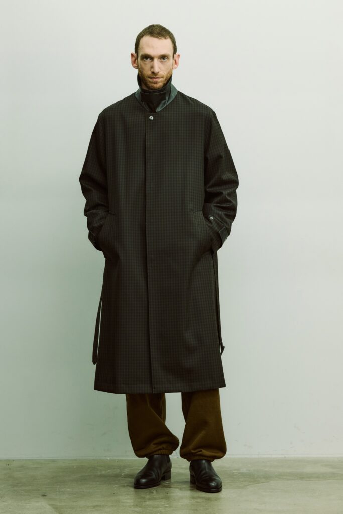 An oversized black coat paired with brown pants, featuring a buttoned front and a relaxed fit.