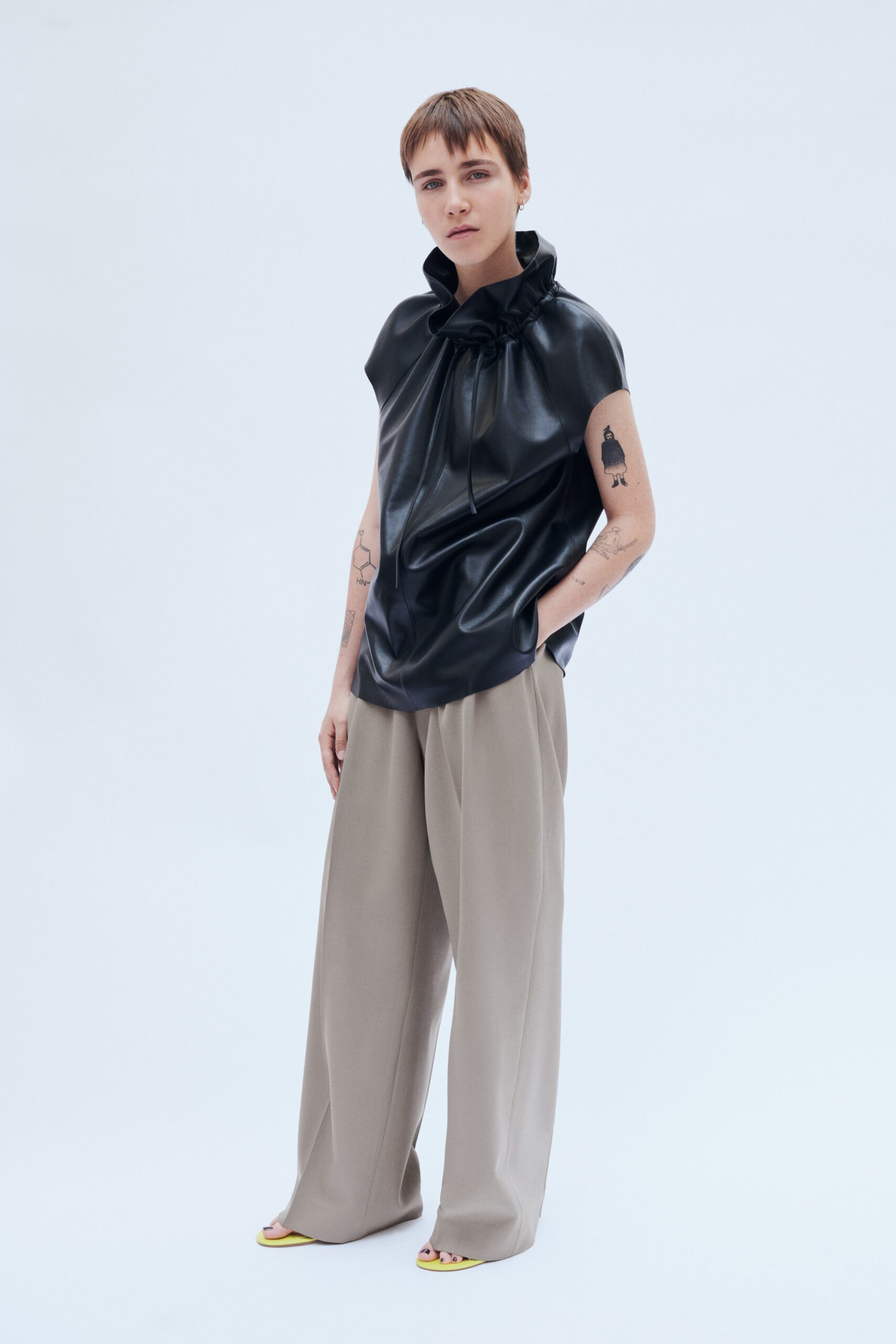 A relaxed black leather sleeveless top with a high neck paired with wide-leg beige pants.