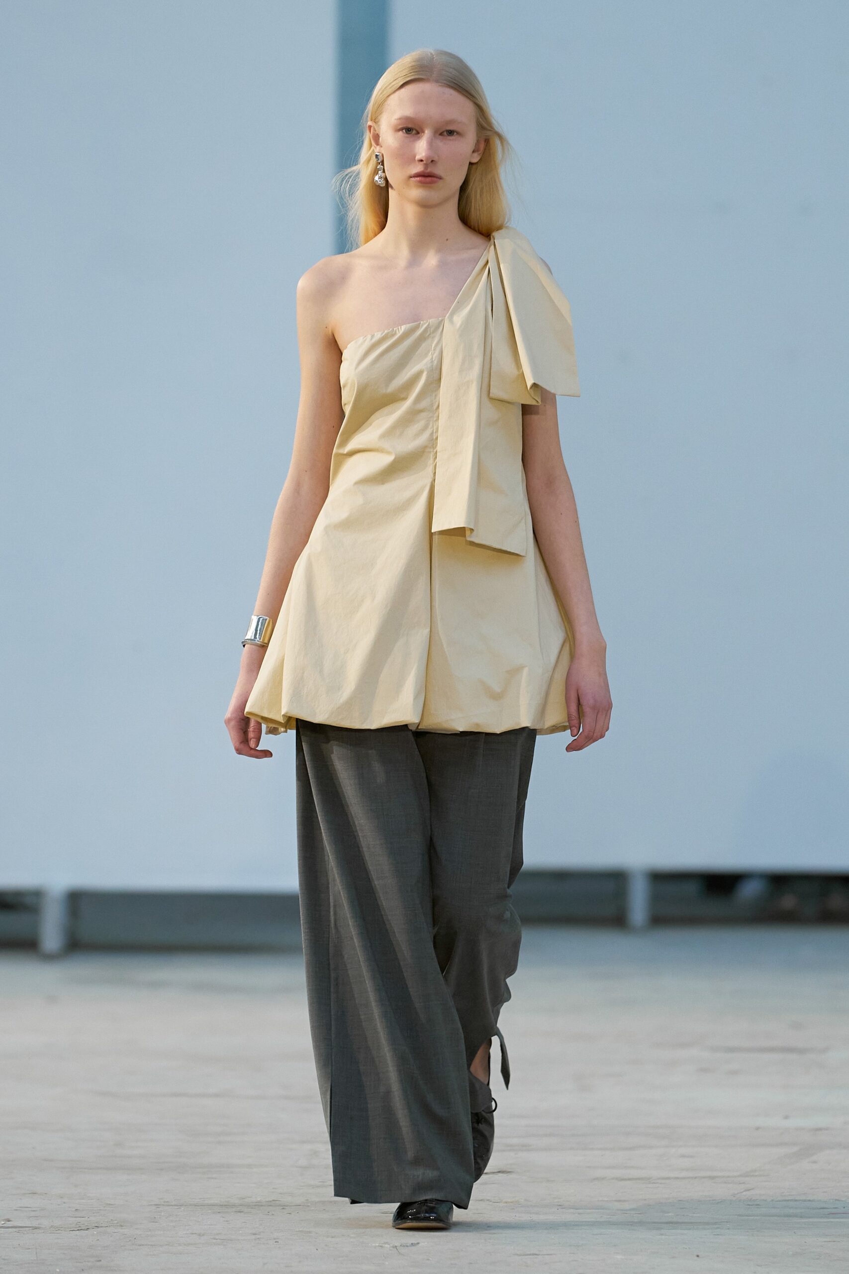 A relaxed beige sleeveless top with pleated details paired with gray relaxed-fit pants.