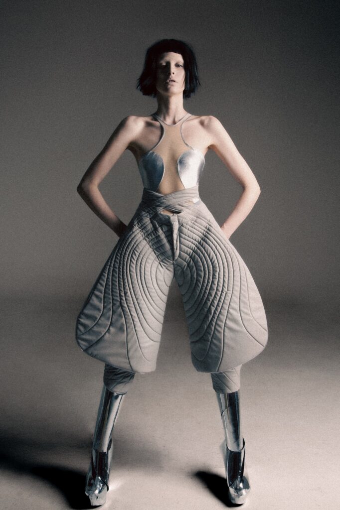 A fitted silver metallic sleeveless top with asymmetric pants, showcasing a unique fashion-forward design.