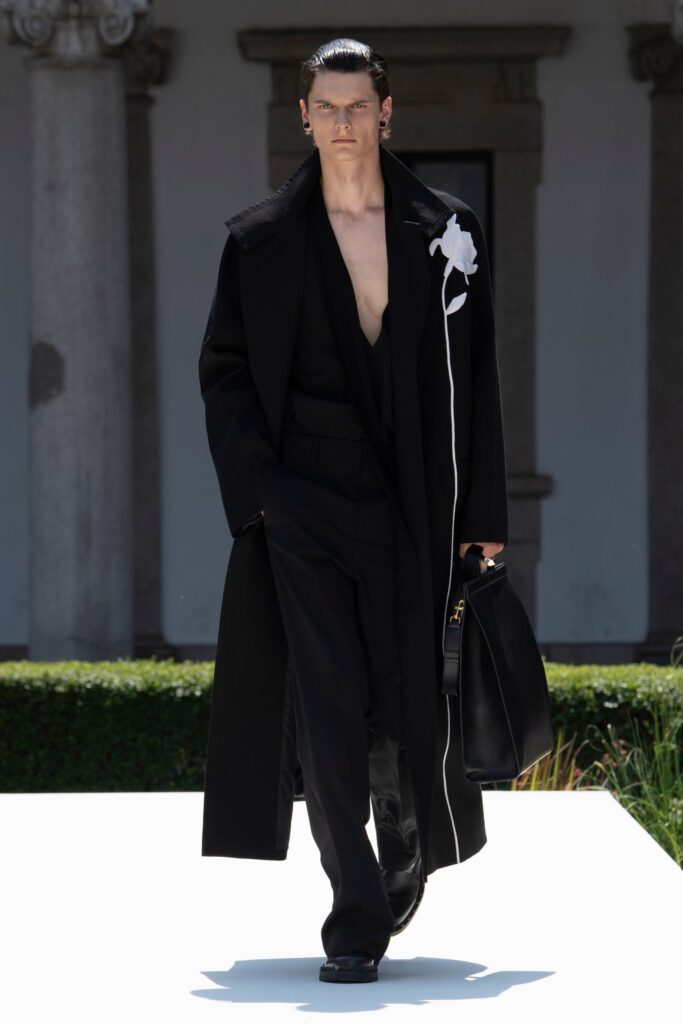 A fitted black wool coat with a V-neck and asymmetric design, paired with tailored pants.