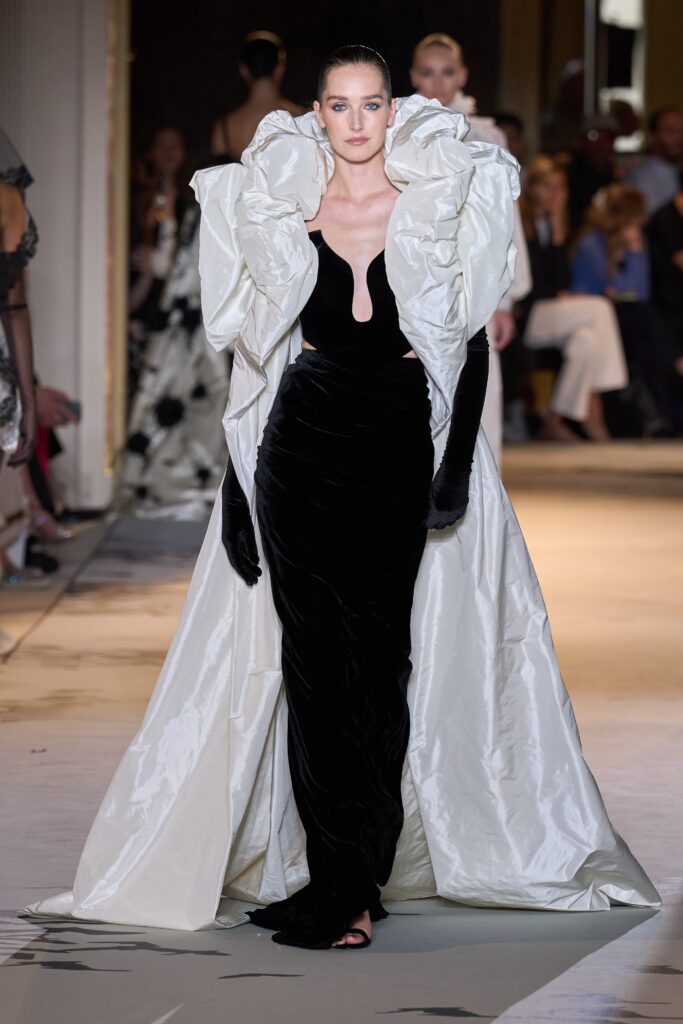 A fitted black velvet sleeveless dress paired with a dramatic white silk coat.