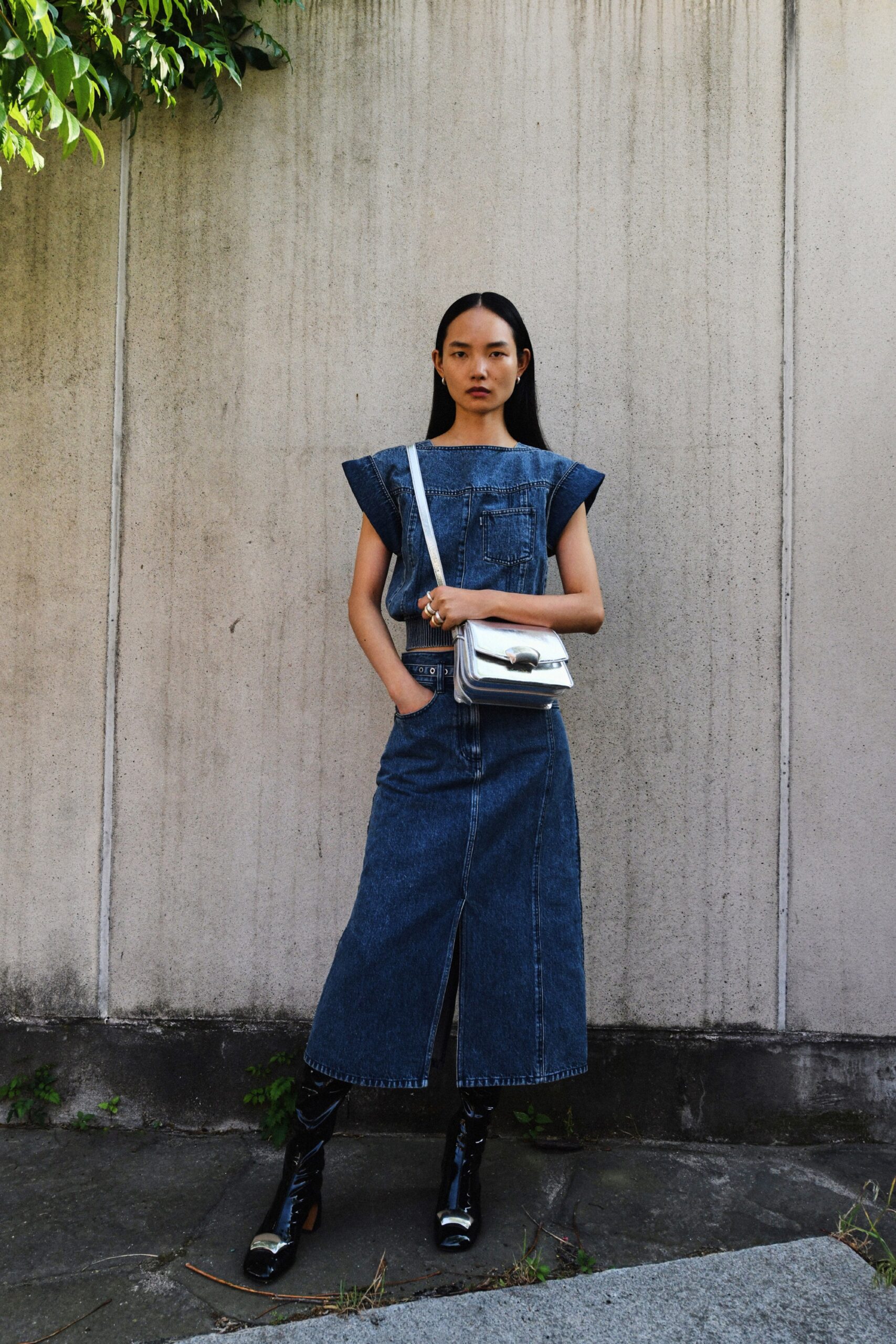 A fitted blue denim sleeveless dress with a high neckline and straight-leg silhouette featuring a slit.