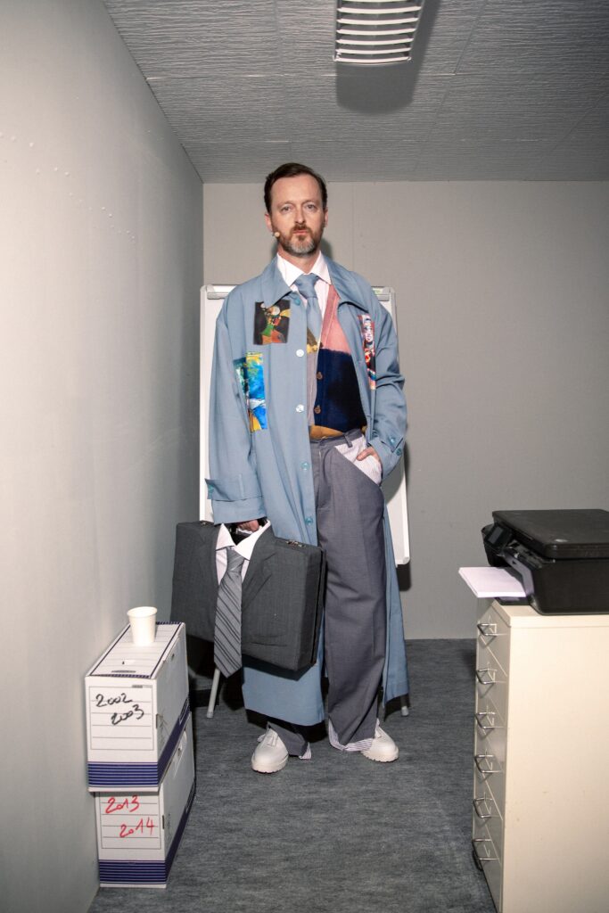 A relaxed blue coat with long sleeves, layered design, and gray pants.