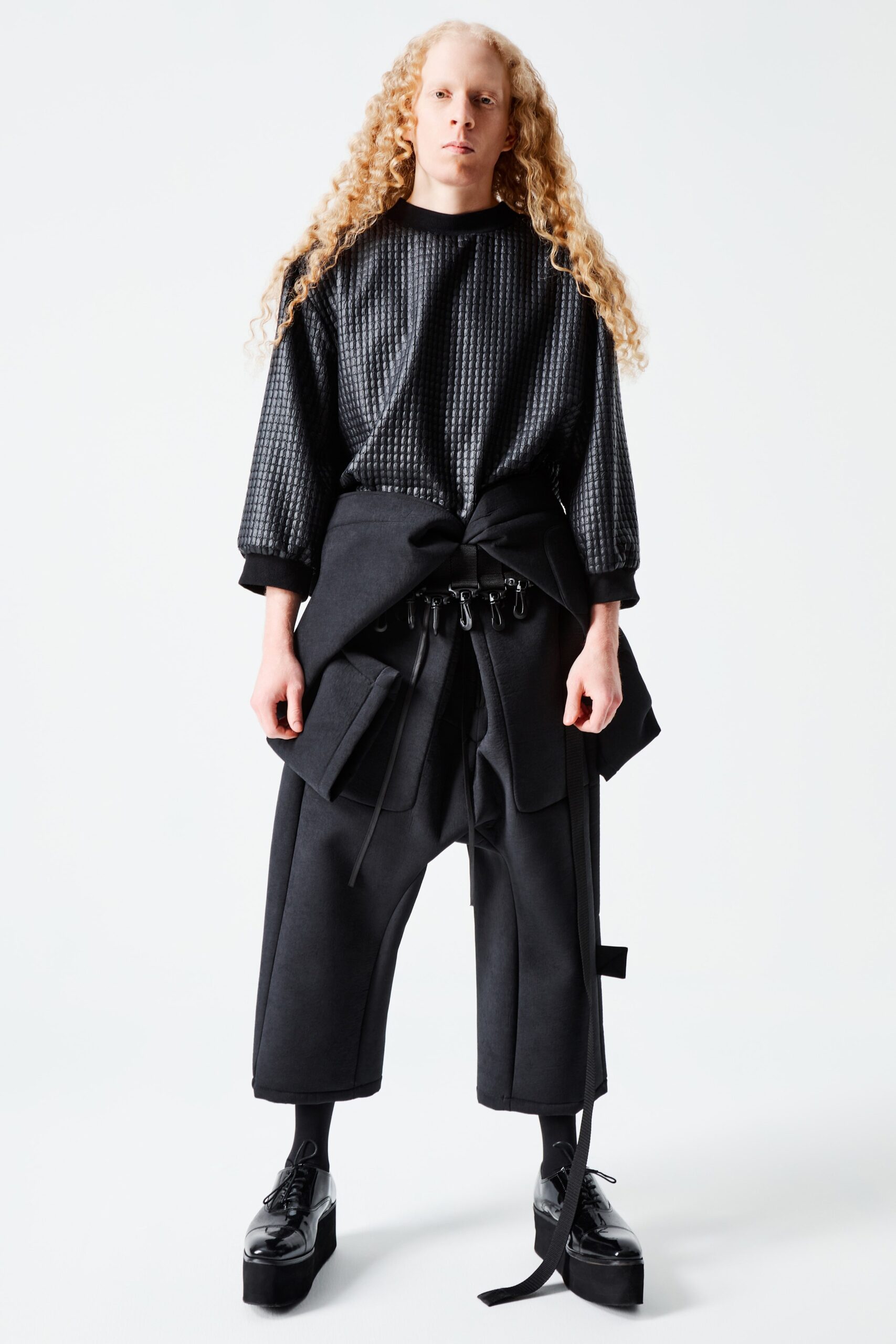 A relaxed top in black cotton features a unique textured surface, complemented by long sleeves and a collared neckline. Paired with matching pants, the layered look creates an intriguing silhouette that balances comfort with contemporary style.