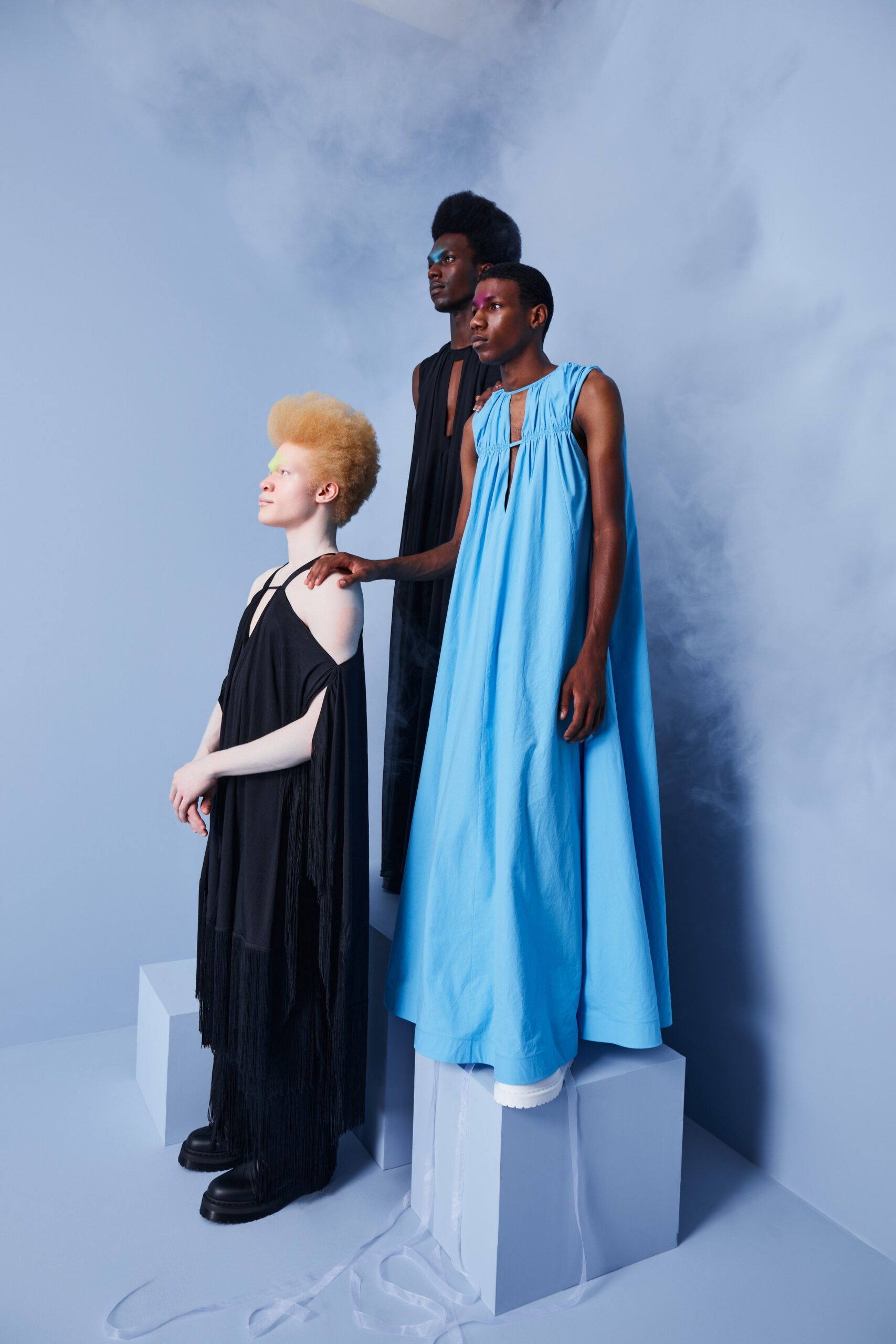 This collection features a relaxed silhouette in both black and blue dresses, showcasing unique high-neck designs. The black dress is adorned with fringed details, while the blue dress offers a flowing, layered effect that creates movement and depth.