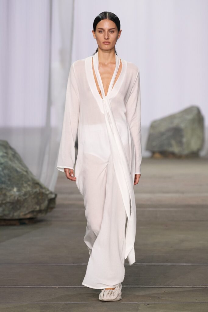 A relaxed white silk dress with long sleeves and a V-neckline featuring an asymmetric design.
