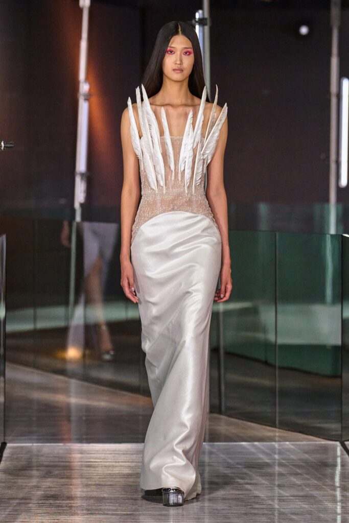 A fitted white silk gown with a high neckline and asymmetric design details.