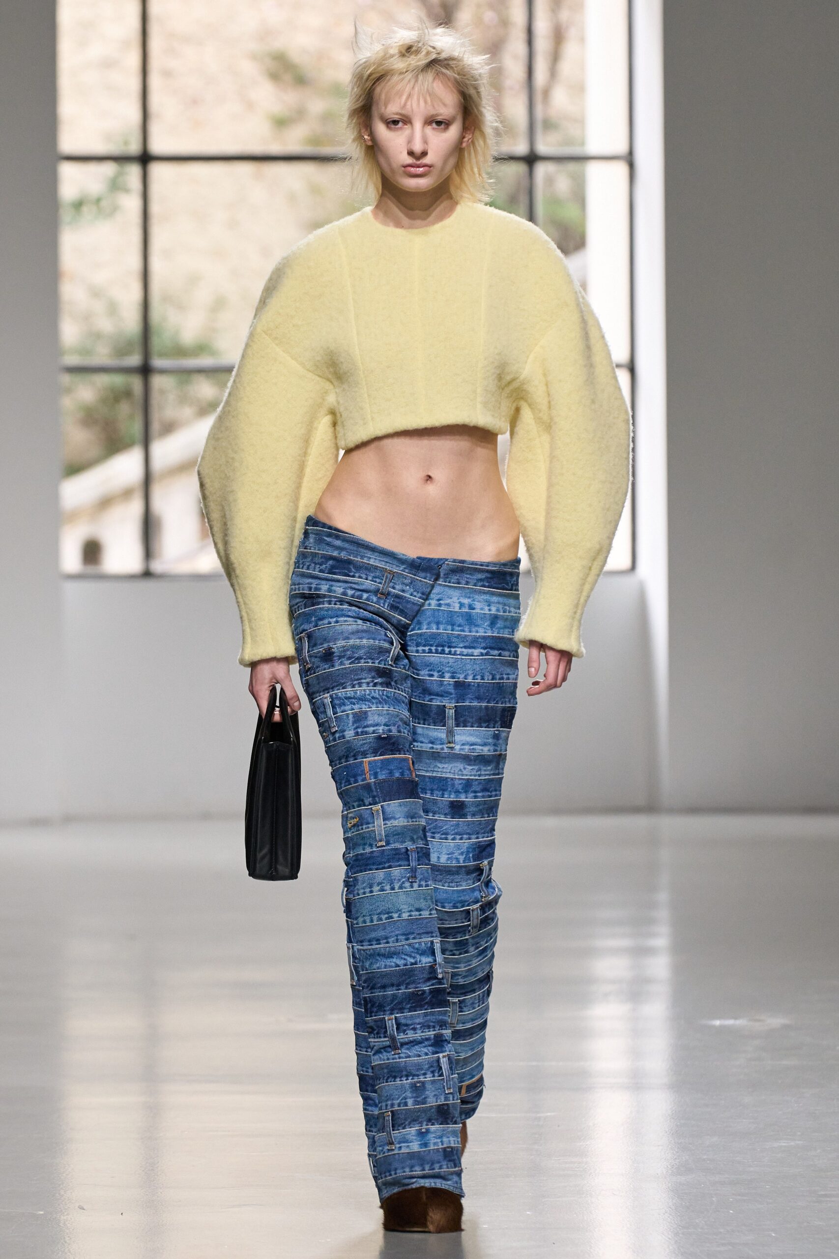 A cropped yellow wool top paired with blue denim pants featuring a layered design.