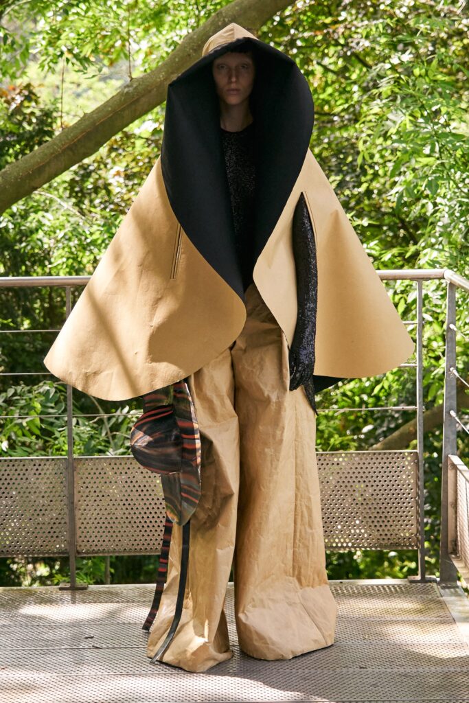 A relaxed beige coat paired with black pants featuring an asymmetric and layered design.
