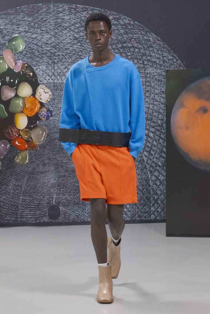 A relaxed blue cotton long-sleeve sweater paired with vibrant orange shorts.