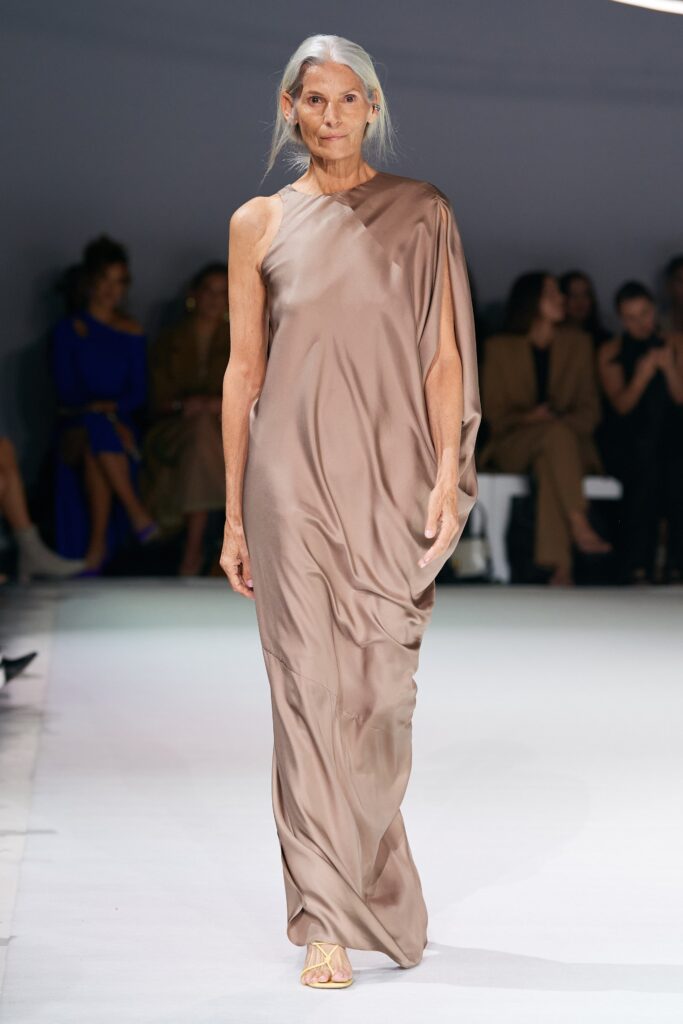 A relaxed beige silk sleeveless dress with a high neckline and draped design.