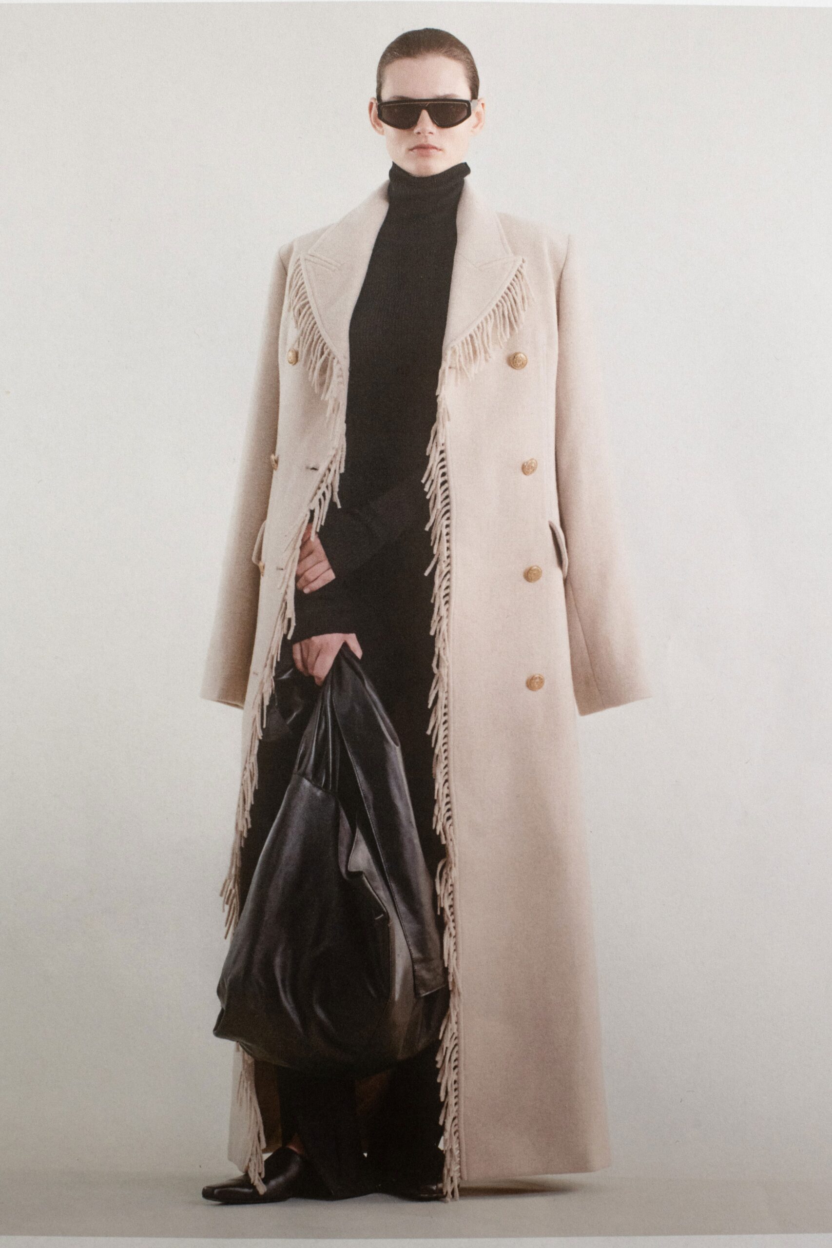 An oversized beige wool coat with long sleeves, a collared neckline, and fringed details.