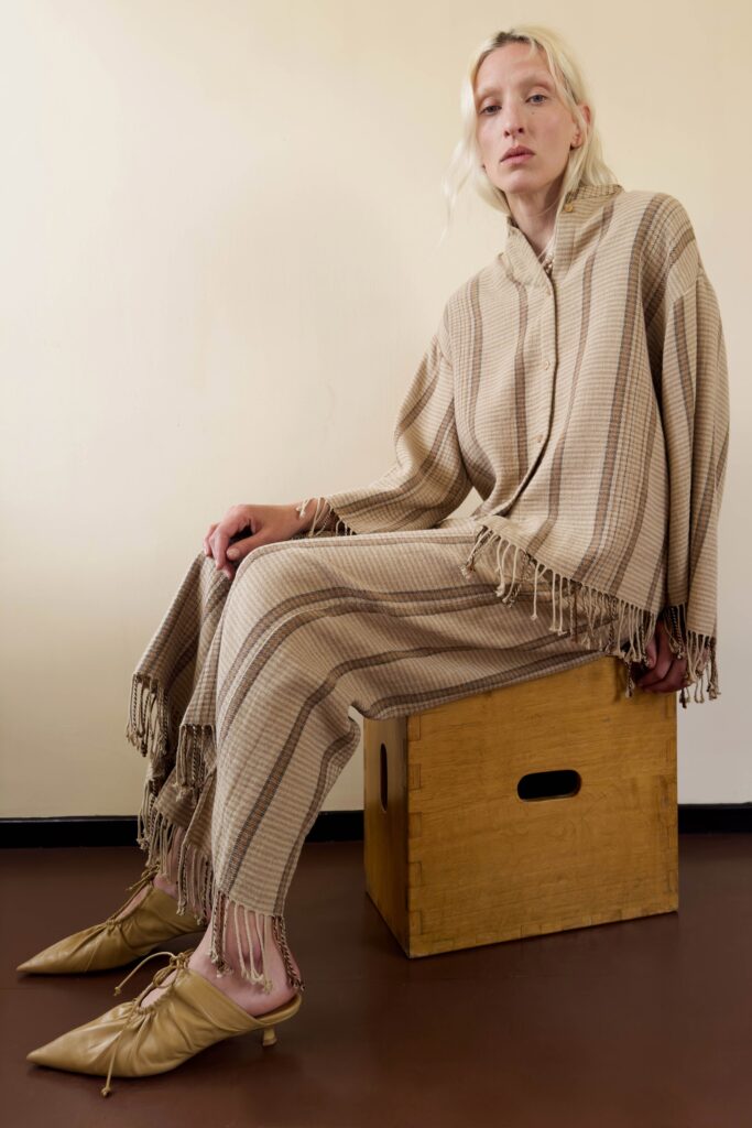 A relaxed beige long-sleeve top with a collared neckline and fringed details paired with matching pants.