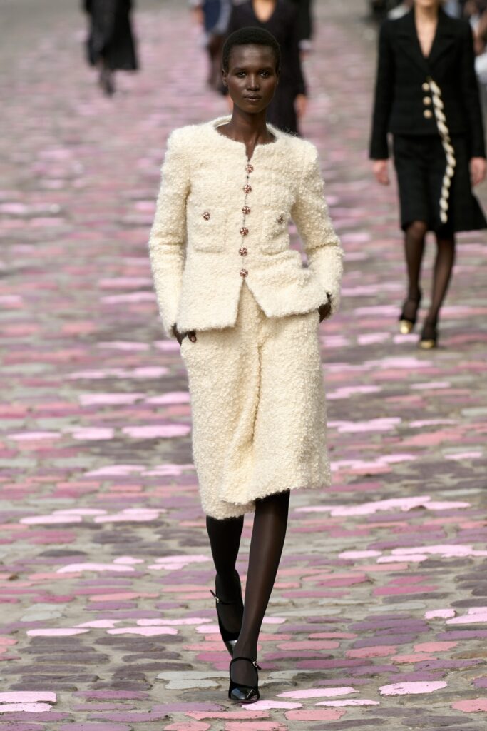A fitted cream tweed suit with a collared long-sleeve jacket and straight-leg trousers.