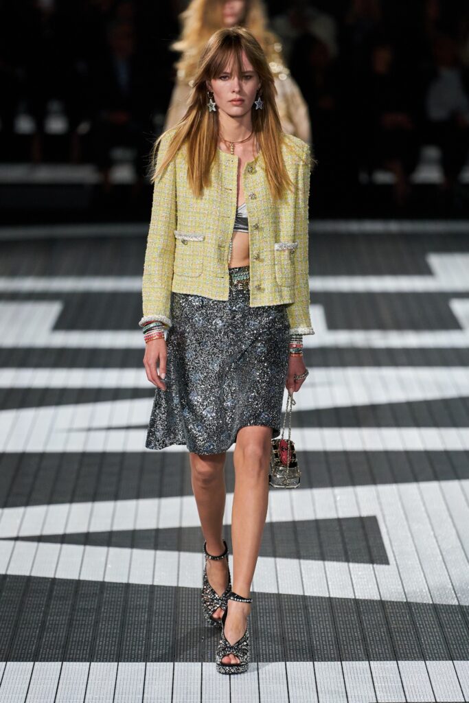 A fitted yellow tweed jacket paired with a pleated silver skirt, showcasing an asymmetric design.