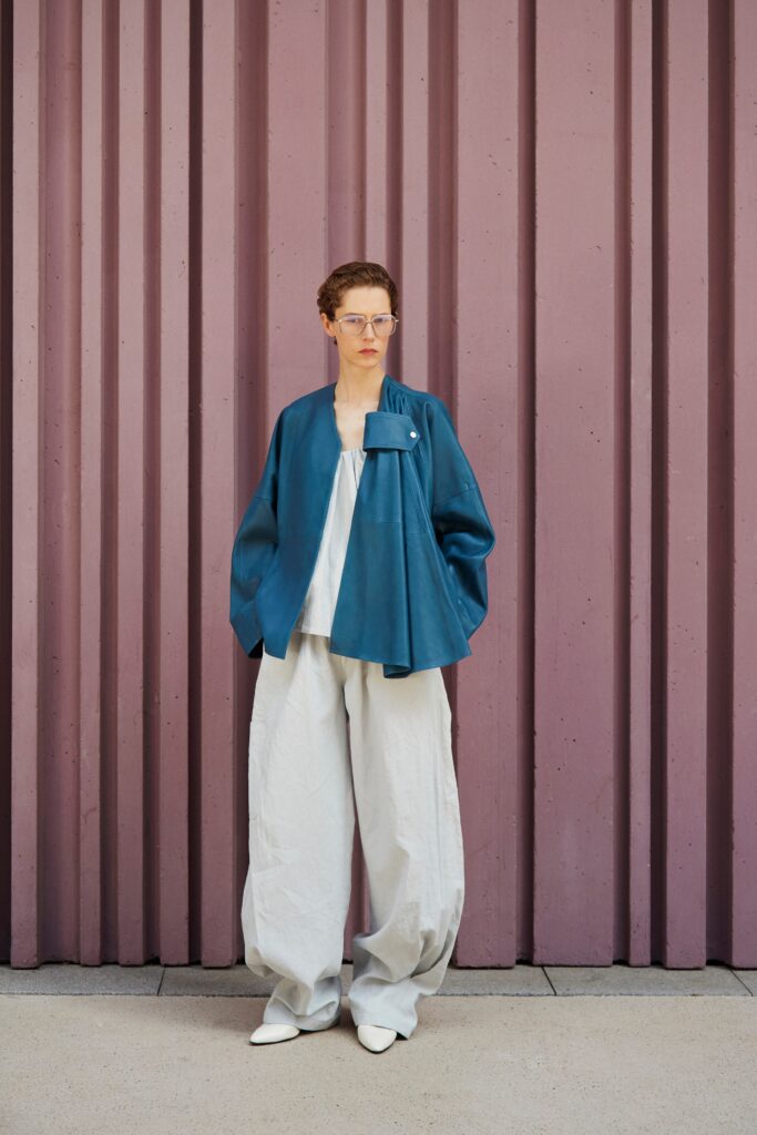 A relaxed blue leather jacket with a collared design paired with wide-leg gray pants.
