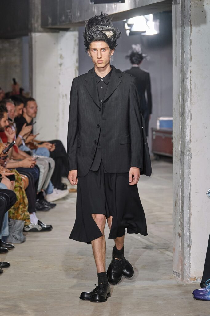 A relaxed black suit with a pleated skirt and long sleeves, featuring an asymmetric design.