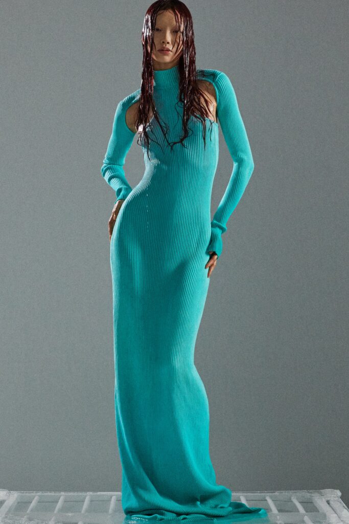 A fitted blue knit dress with long sleeves, a high neckline, and a stylish slit.