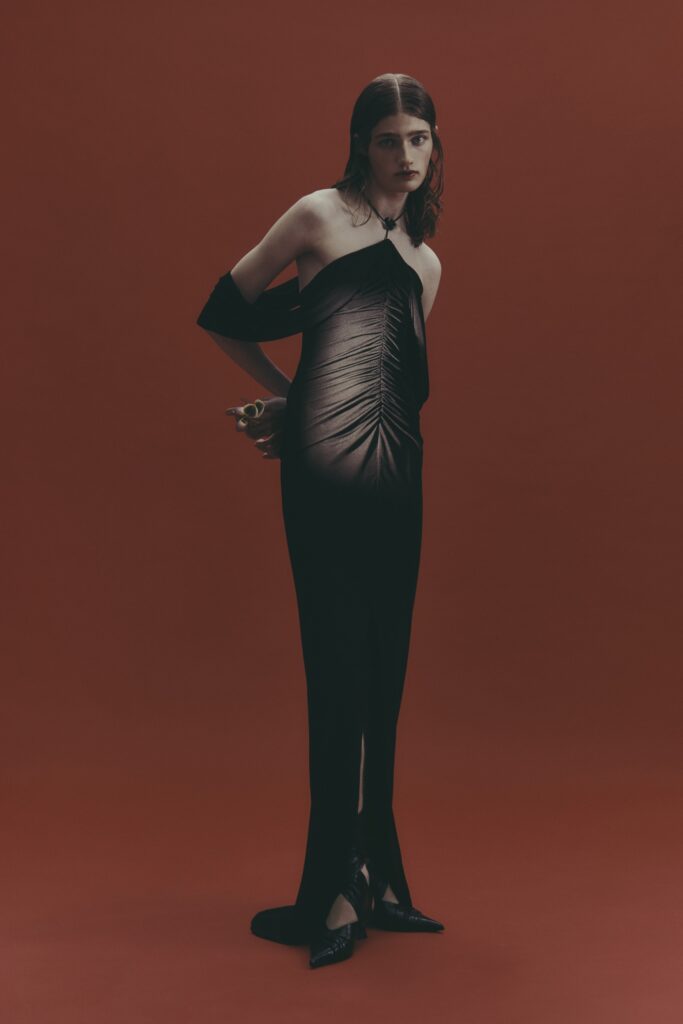 A fitted black silk dress with an off-shoulder design and draped detailing.