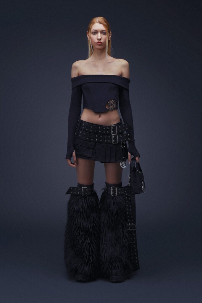 A fitted black off-shoulder top with long sleeves paired with a pleated skirt featuring fringed details.