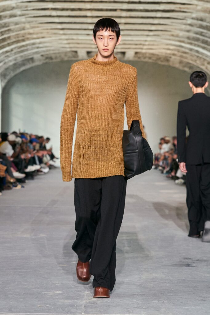 A relaxed brown knit sweater with long sleeves and a high neck, paired with straight-leg black pants.