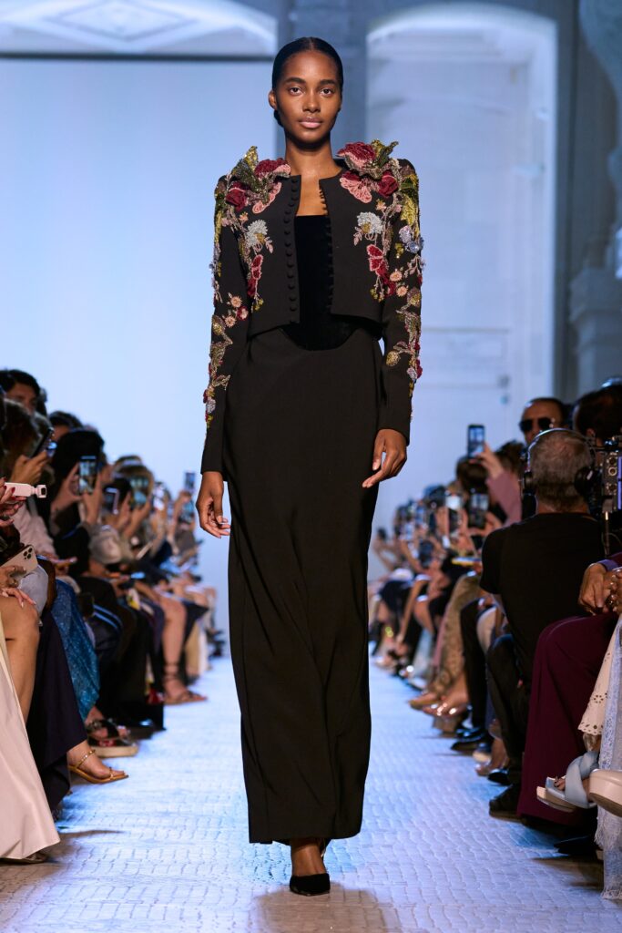 A fitted black silk dress with long sleeves and an embroidered jacket, creating an elegant silhouette.
