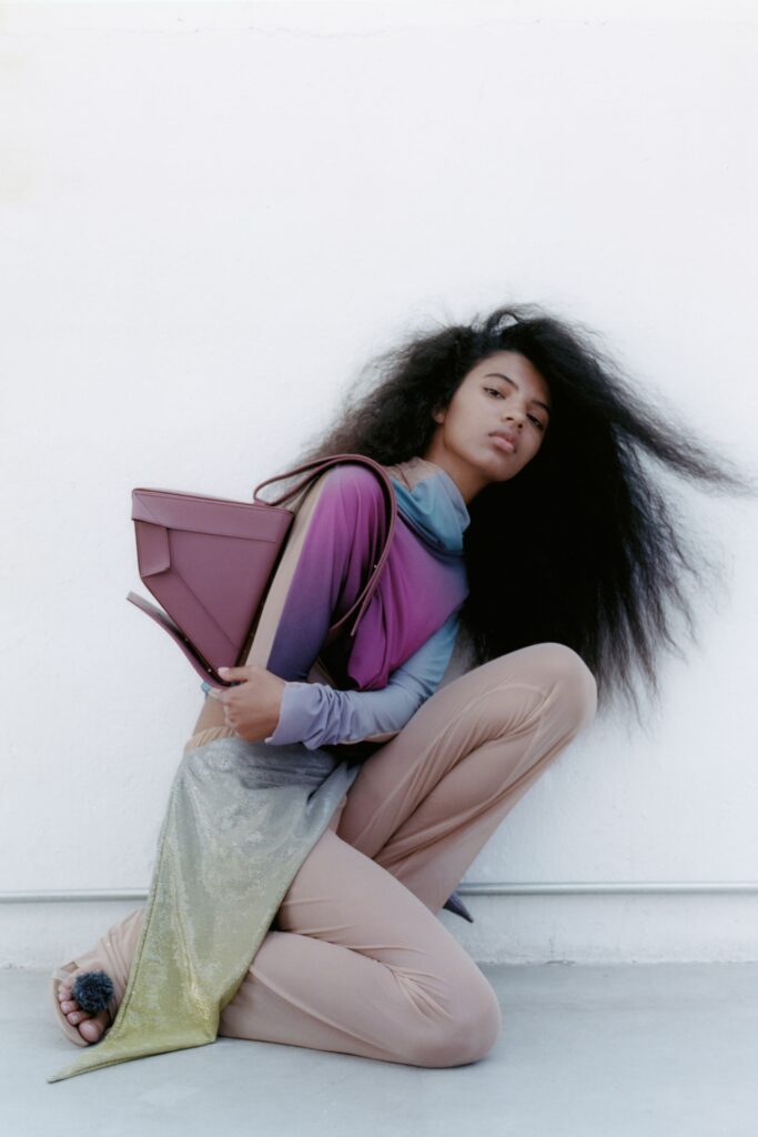 A fitted purple silk long-sleeve top with a high-neck and asymmetric design paired with beige pants.