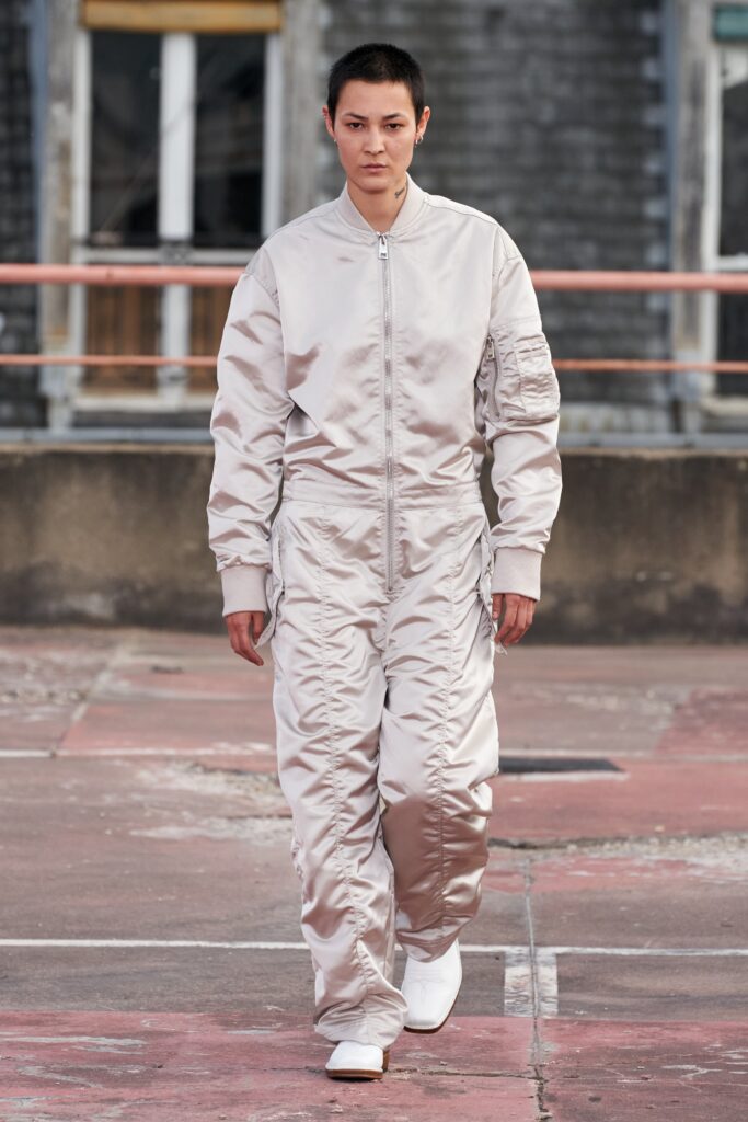 A relaxed beige jumpsuit with long sleeves and pleated details, featuring a zippered front.