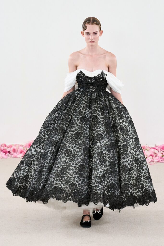 A fitted black and white lace dress with an off-shoulder design and tiered silhouette.
