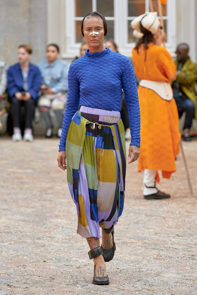 A relaxed blue long-sleeve top paired with a colorful striped skirt featuring an asymmetric design.