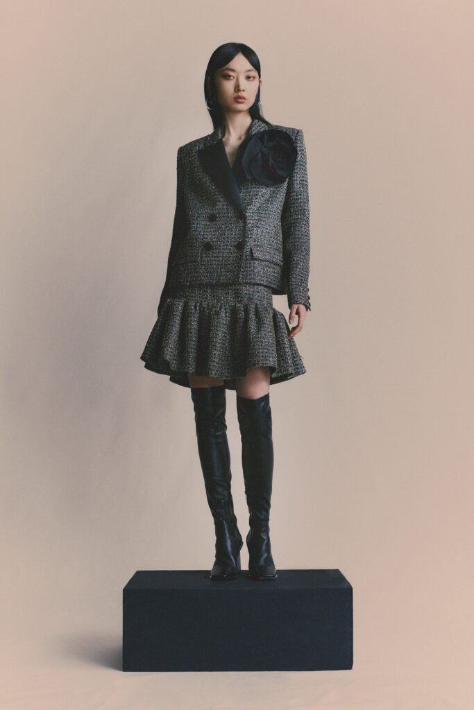 A fitted gray tweed blazer with a ruffled skirt, featuring long sleeves and a collared design.