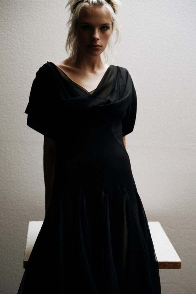 A fitted black silk dress with a V-neckline and flared silhouette.