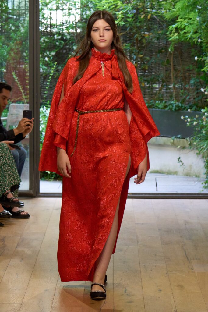 A fitted red silk dress with a high-neck and layered cape, featuring a slit detail.