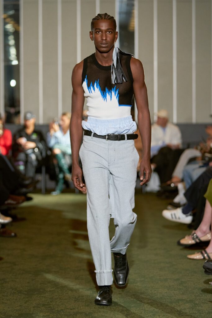 A fitted sleeveless top with an asymmetric design and printed details paired with gray pants.