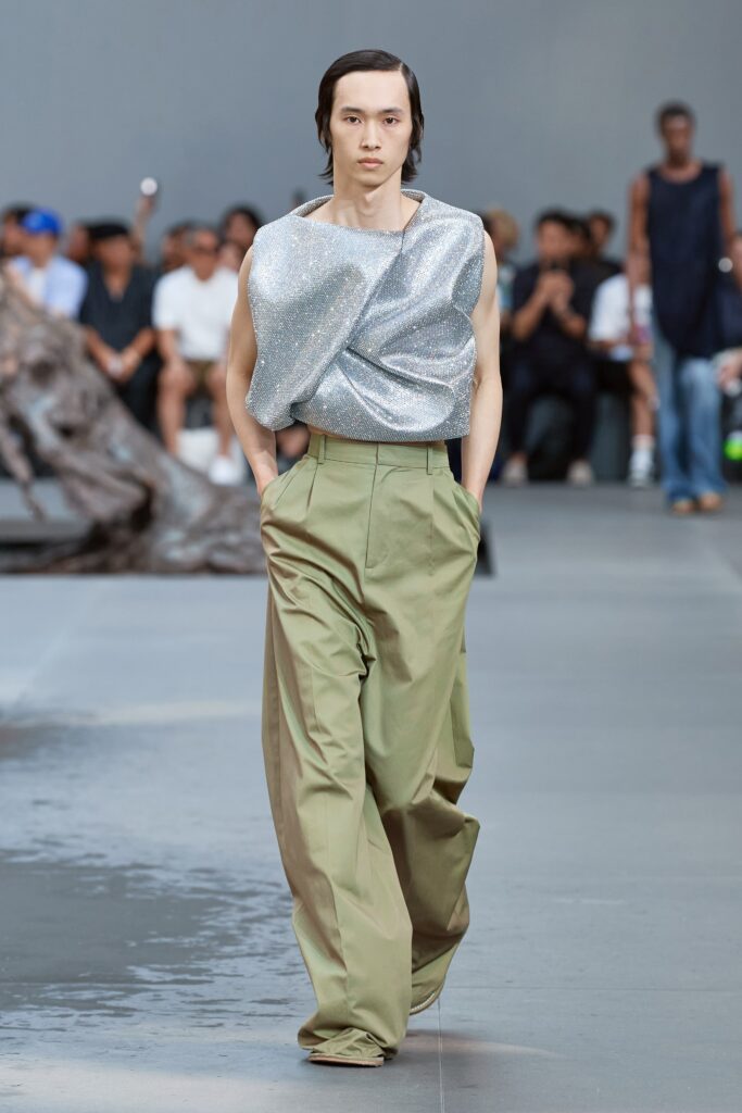 A relaxed silver sleeveless top with an asymmetric design paired with wide-leg green pants.