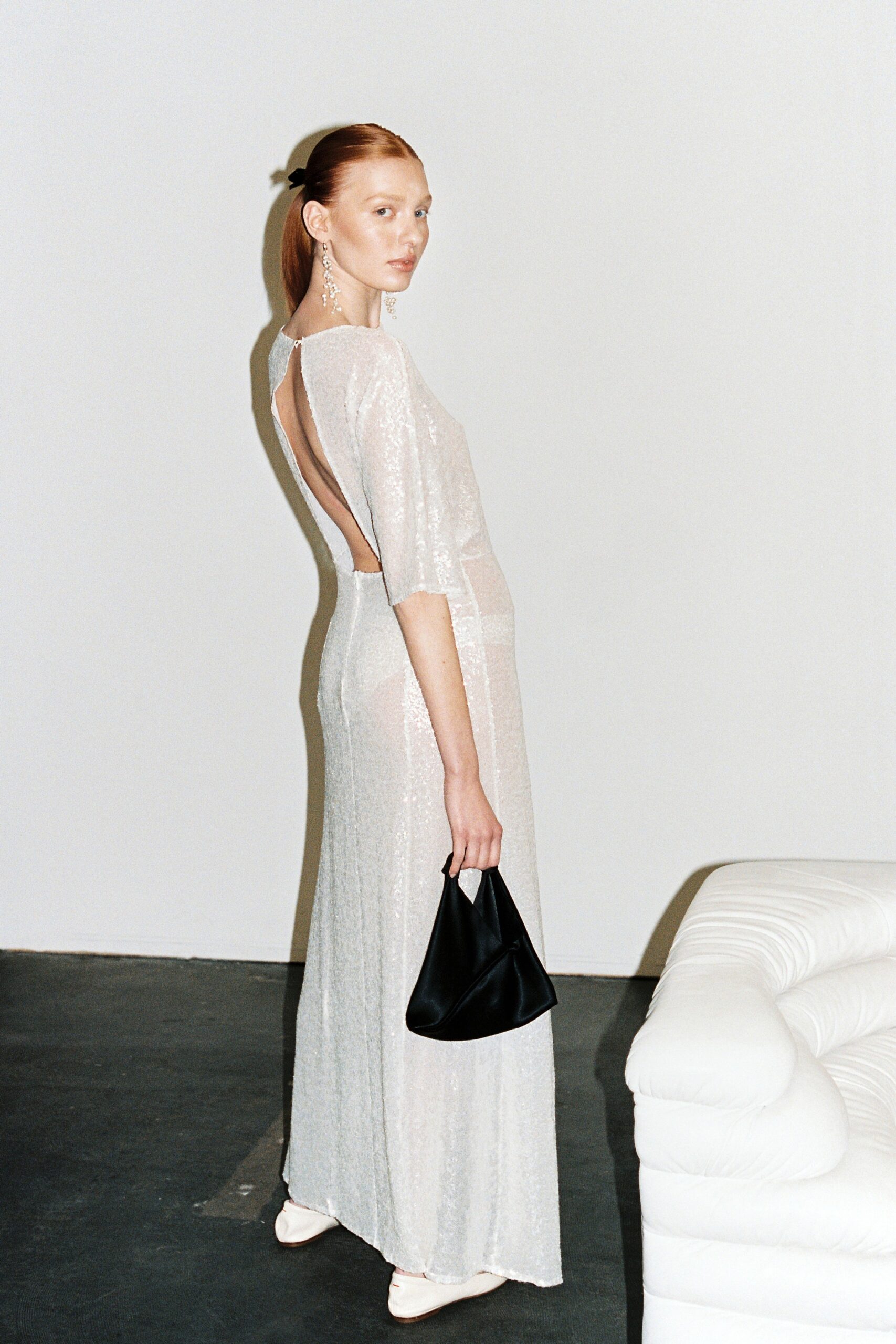 A fitted white silk gown with long sleeves and a backless design featuring sheer elements.