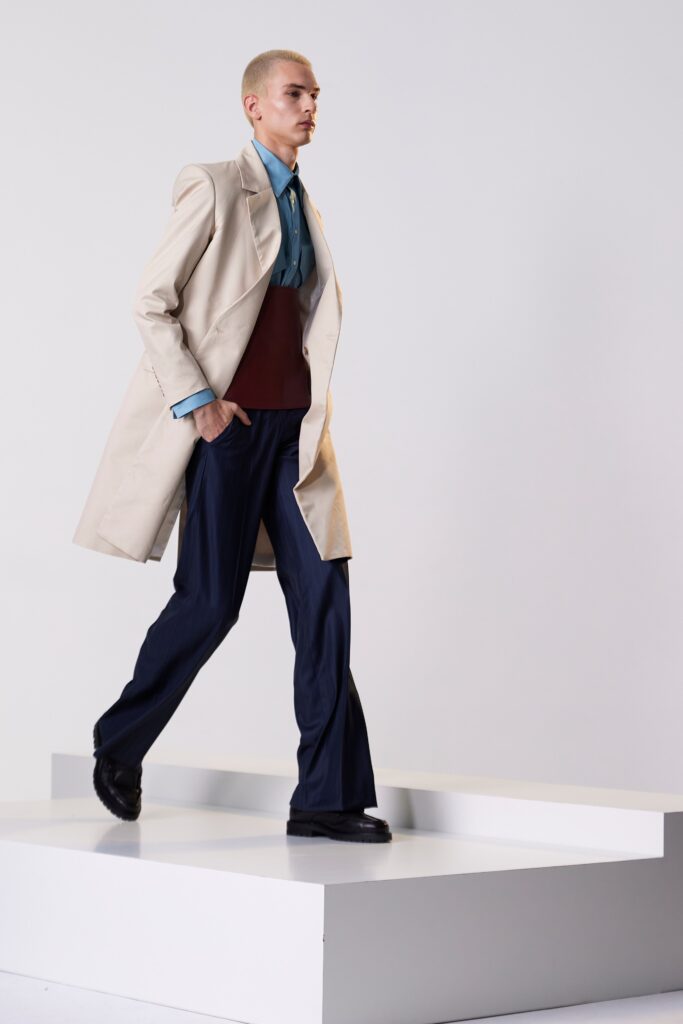 A relaxed-fit beige coat paired with navy straight-leg pants and a collared shirt.