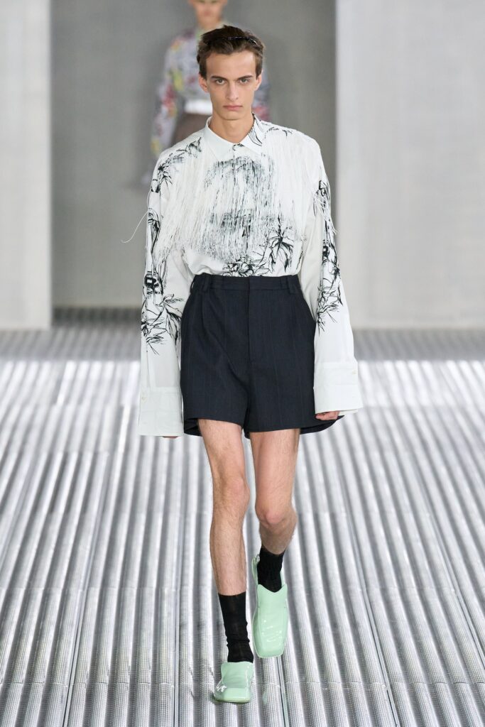 A fitted white printed long-sleeve shirt paired with tailored black shorts.