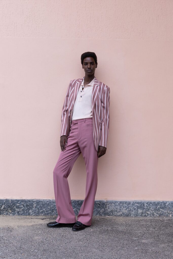 A fitted pink striped blazer paired with white collared shirt and flared pink pants.