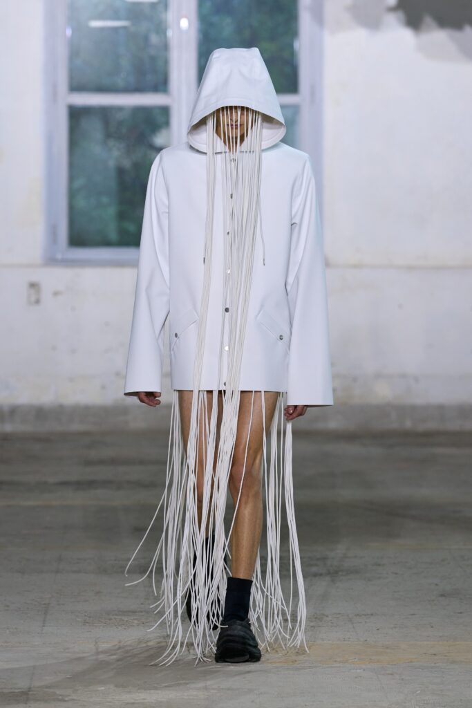 A relaxed white hooded coat with an asymmetric design and unique fringe detailing.