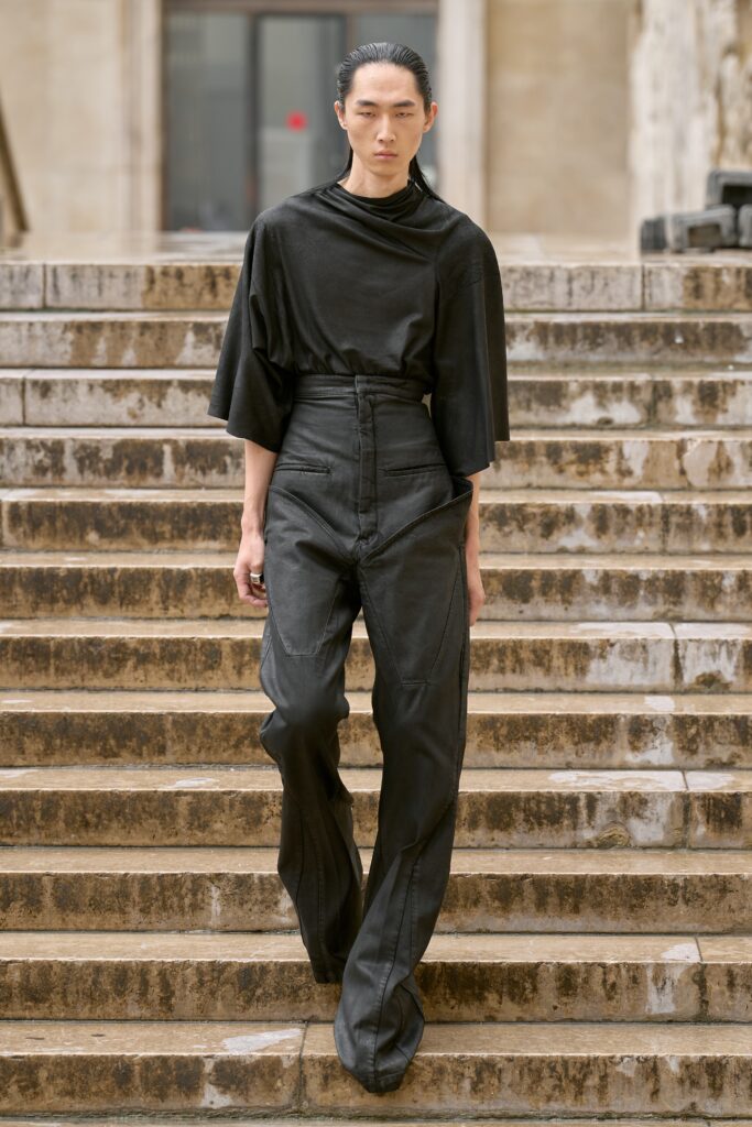 A relaxed black top with a high neck paired with wide-leg black pants.