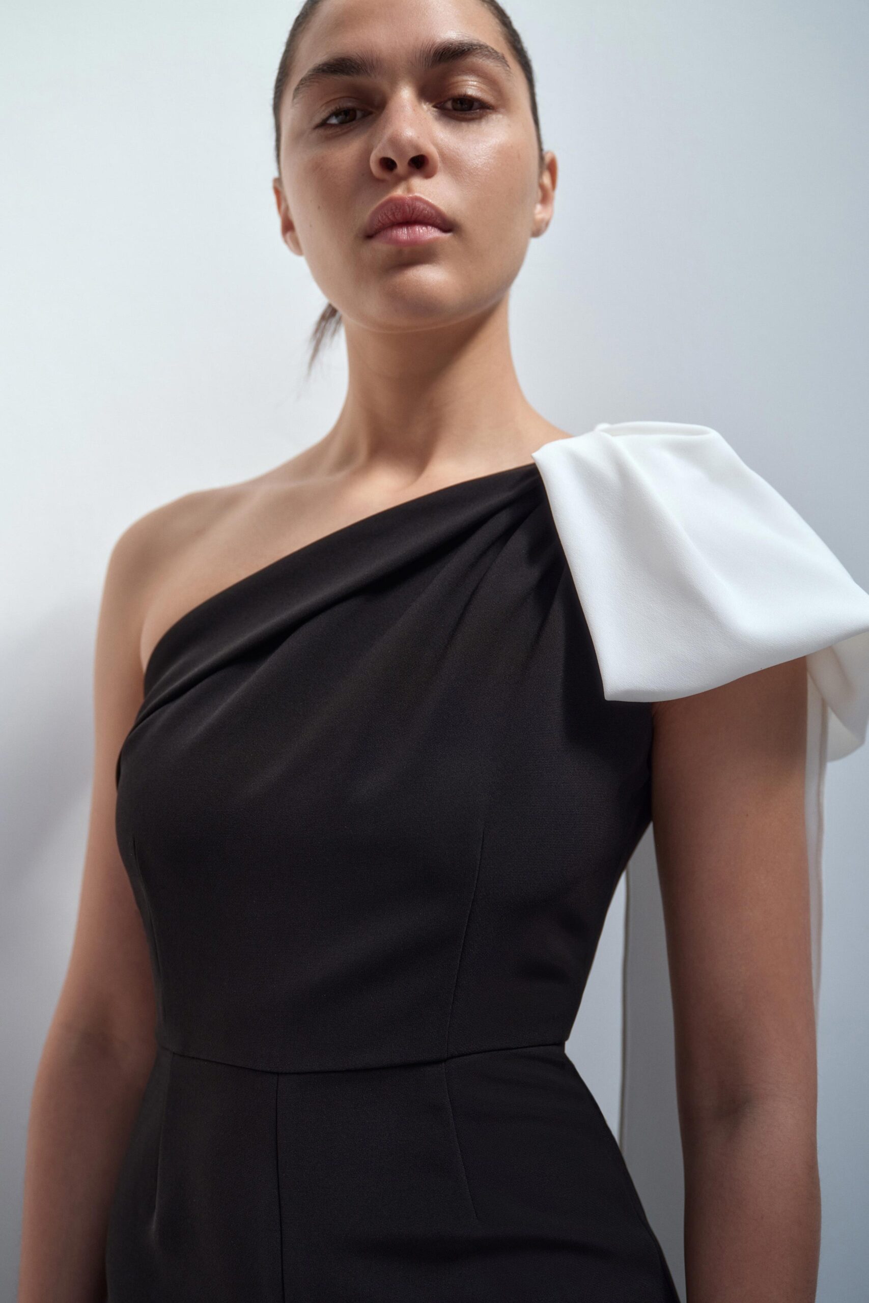 A fitted black dress with a white bow detail and an asymmetric design.