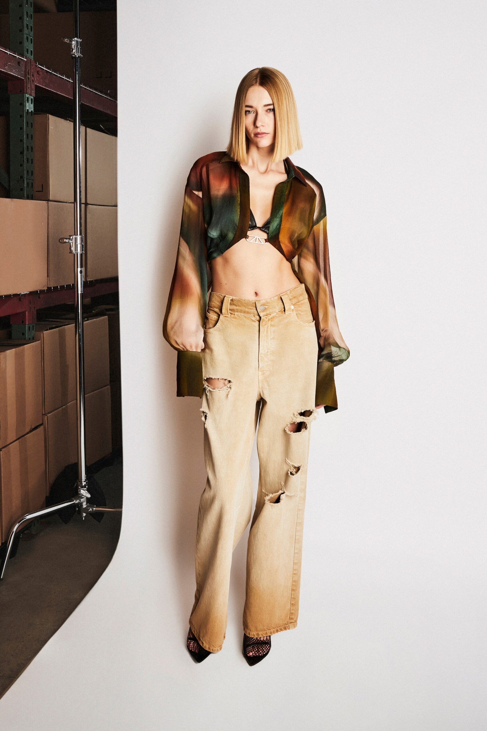 A relaxed multicolor long-sleeve shirt layered over a casual pair of ripped beige pants.