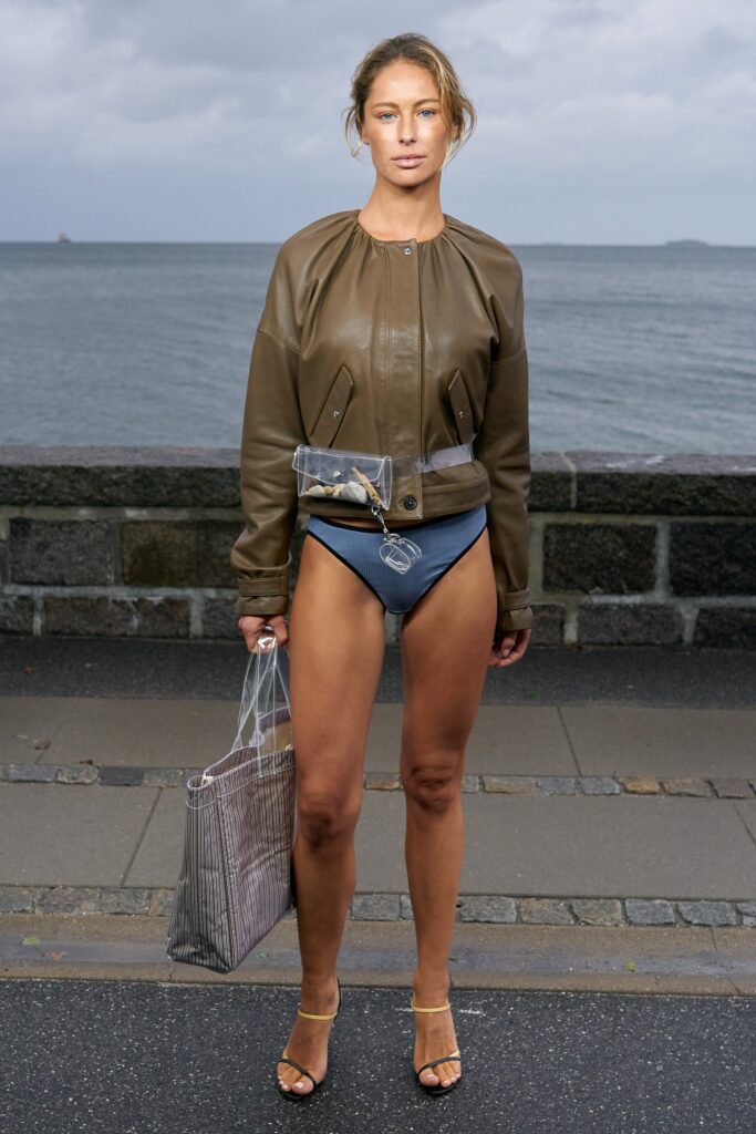A fitted brown leather jacket paired with a blue bikini, showcasing a stylish beach look.