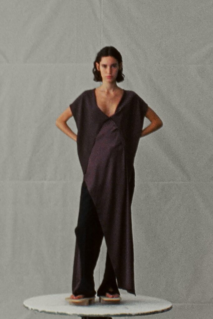 A relaxed black sleeveless dress with a V-neckline and asymmetric design paired with pants.